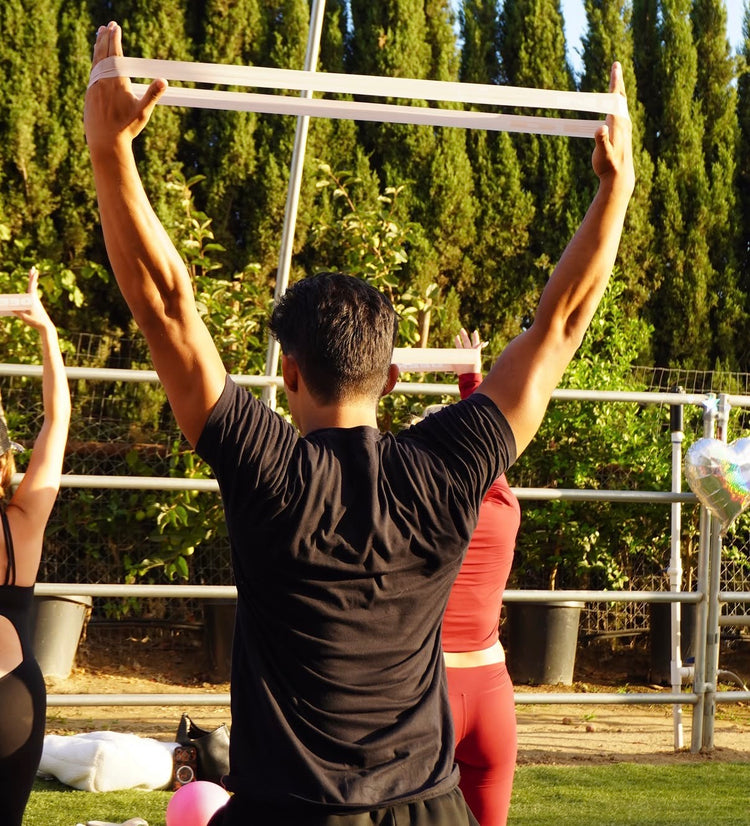 A guest stretching a resistance band overhead during an outdoor class