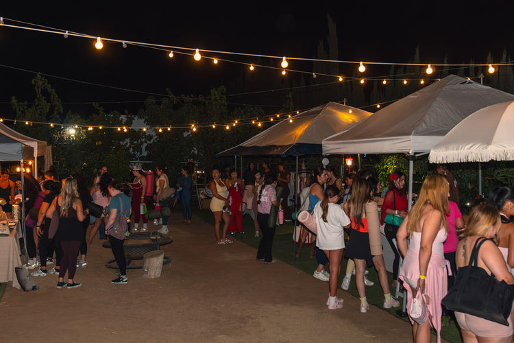 A crowd mingling under glowing string lights at an evening social