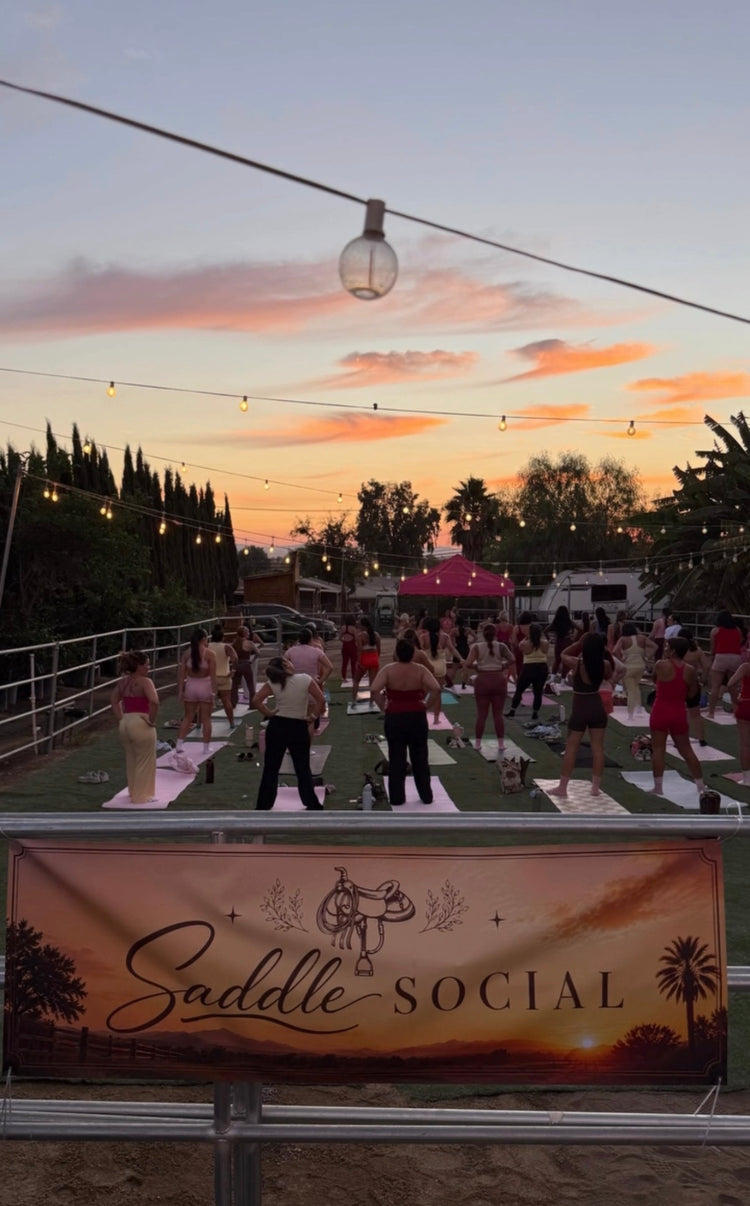 Sunset Pilates class under string lights behind a Saddle Social banner